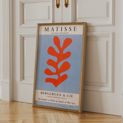 A framed poster of the Métisse art movement, featuring a large orange abstract leaf design, is leaning against a white door.