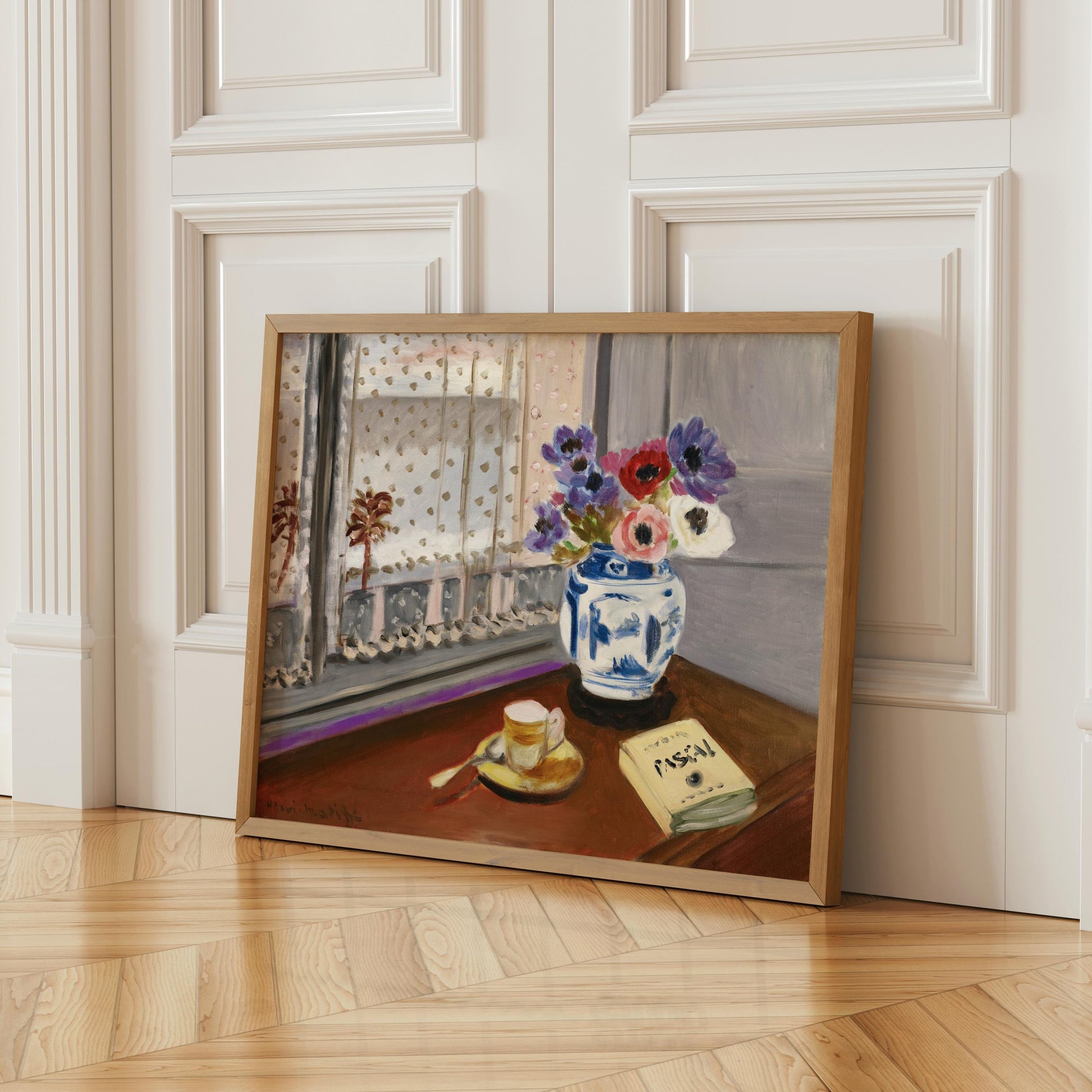 A framed painting depicting a vase of flowers on a table, with a book and a cup of coffee nearby, set against a window with a white curtain.