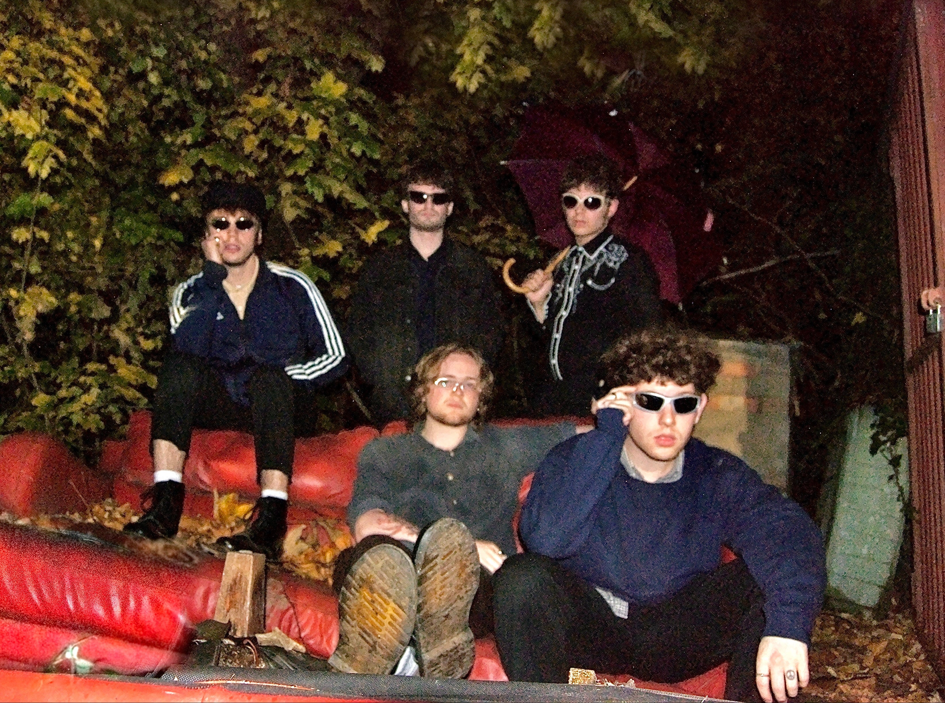 Four people sitting on a red couch outdoors with trees in the background