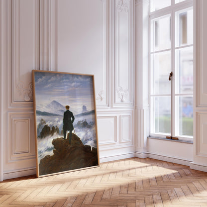 a large painting of a person standing on a rocky cliff, overlooking a misty landscape. The painting is displayed on a white wall in a room with a large window, allowing natural light to illuminate the artwork.