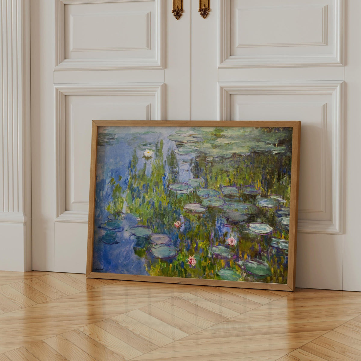 A framed painting of a water lily pond is displayed on a wooden floor against a white door.